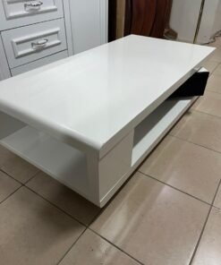 A modern coffee table in glossy white with a black lower drawer featuring a distinctive geometric design.