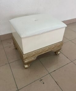 A small stool designed in a classic style, featuring a white top with gold details and an ornate base.