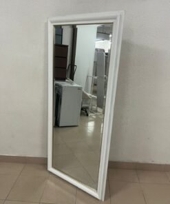 A freestanding mirror with a wide white frame and gold inner edges.