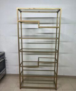 Metal shelving unit with a geometric design and gold frame, featuring transparent glass shelves.