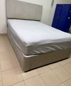 A light beige upholstered bed with a long, padded headboard.