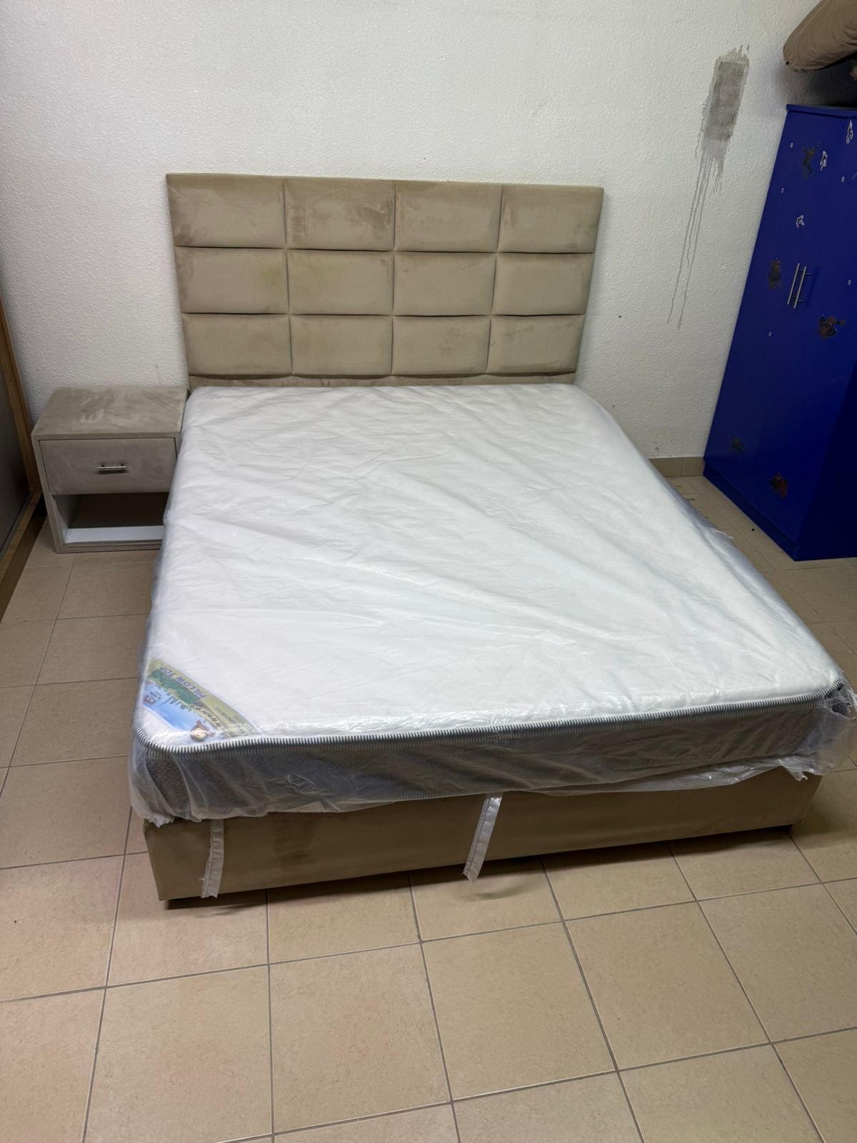 The beige upholstered bed features a checkered, padded headboard and comes with a new mattress. - Image 9
