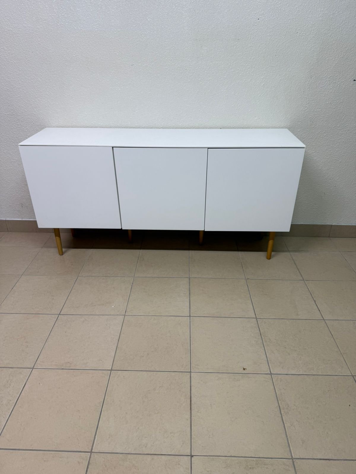 A modern white buffet cabinet featuring a simple design and light-colored wooden legs.