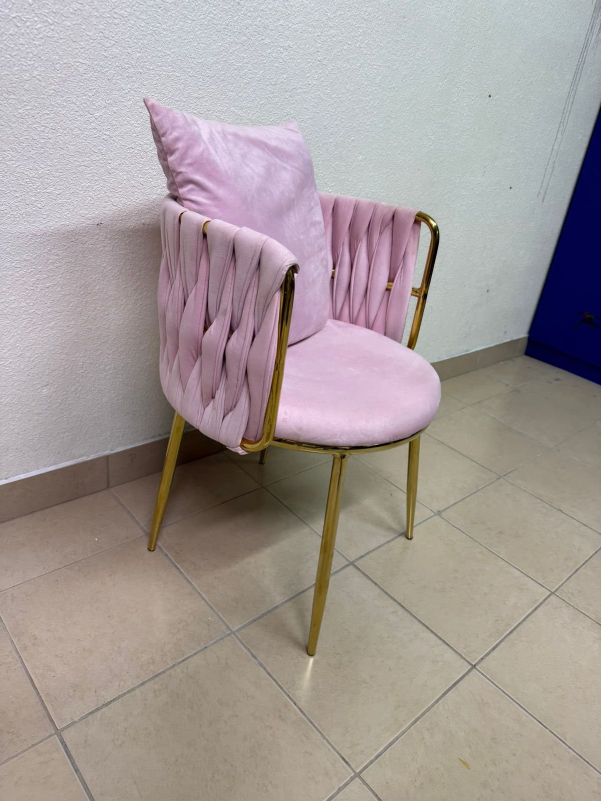 The pink velvet chair features a modern design with a woven back and an elegant gold metal base.