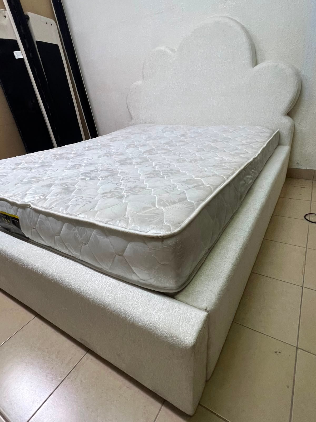 A fully upholstered white frame bed featuring a unique cloud-shaped headboard design.