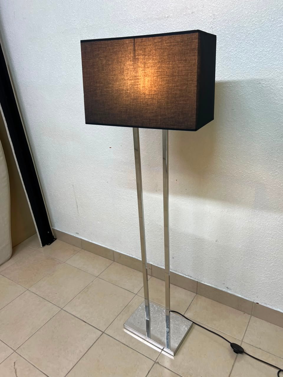 This modern floor lamp features a chrome-plated metal frame and a black fabric cover.