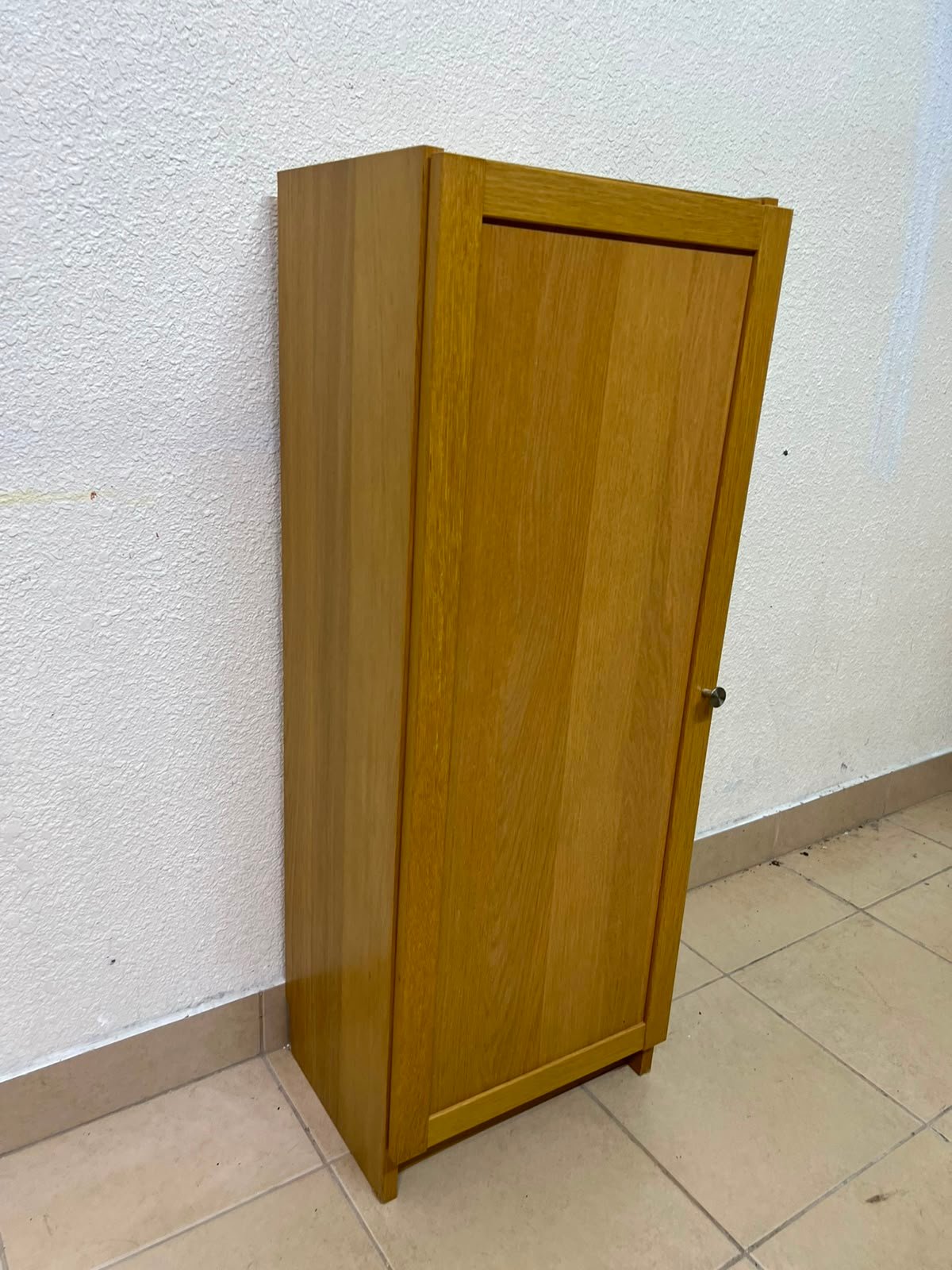 A narrow storage cabinet, either IKEA-style or similar, featuring a natural oak veneer finish.