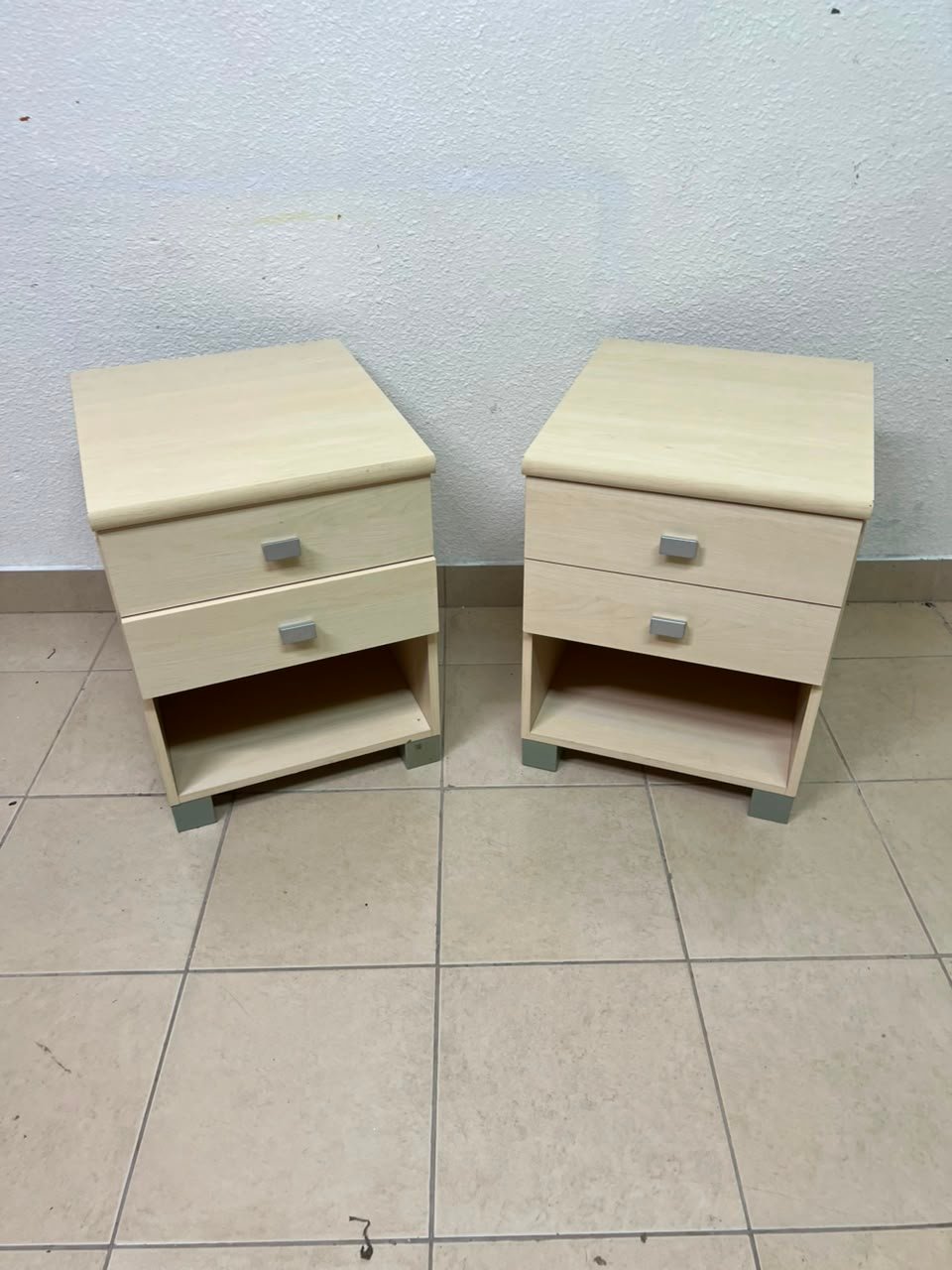 A set of two modern bedside tables in a light wood color with two drawers and open storage space.