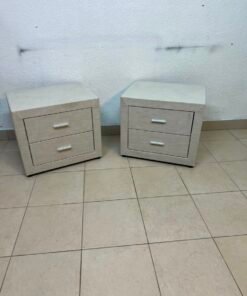 A beige upholstered nightstand with two drawers and silver handles.