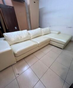 A modern L-shaped white leather sofa featuring a wide armrest and comfortable back cushions.