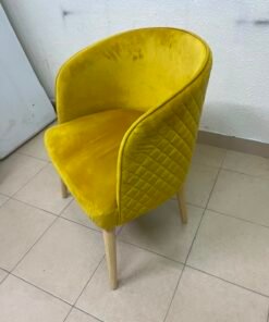 The modern chair features luxurious yellow velvet upholstery, a curved back with a padded design on the sides, and sturdy wooden legs.