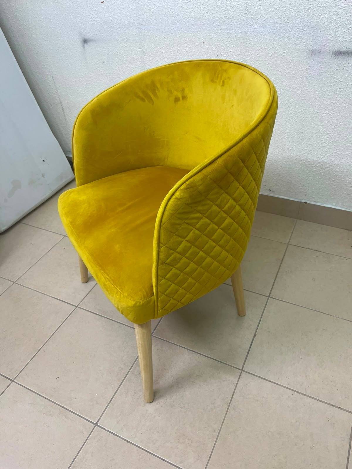 The modern chair features luxurious yellow velvet upholstery, a curved back with a padded design on the sides, and sturdy wooden legs.