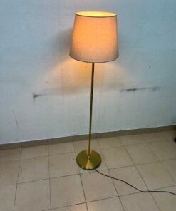 A modern and elegant floor lamp (lampade) with a slim, copper-gold metal base and a warm fabric shade.