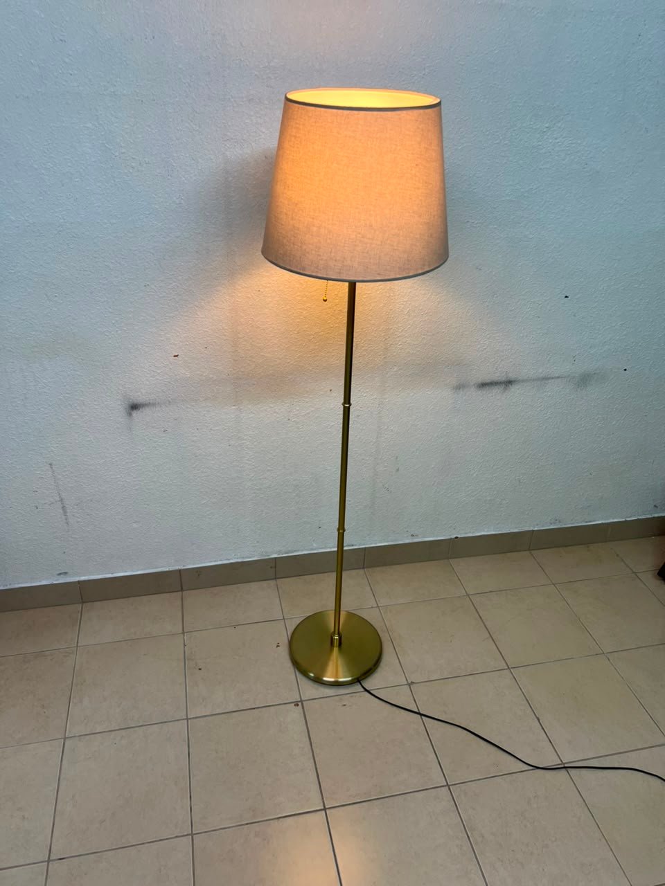 A modern and elegant floor lamp (lampade) with a slim, copper-gold metal base and a warm fabric shade.