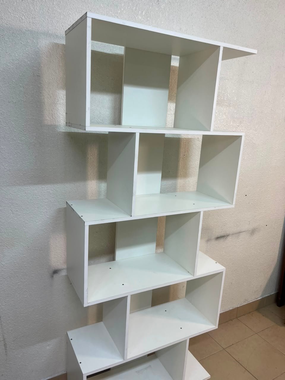 This white 5-tier geometric S-shaped bookshelf functions as an open display rack or room divider.