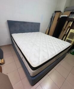 A modern, gray, upholstered double bed, paired with a thick, padded mattress with a soft top layer, featuring a prominent black border.