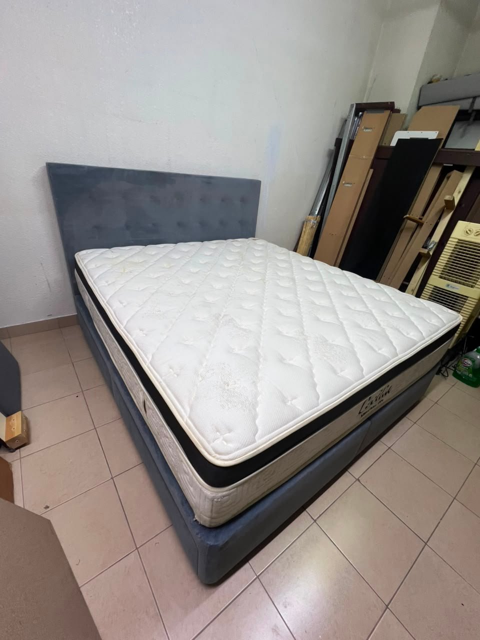 A modern, gray, upholstered double bed, paired with a thick, padded mattress with a soft top layer, featuring a prominent black border.