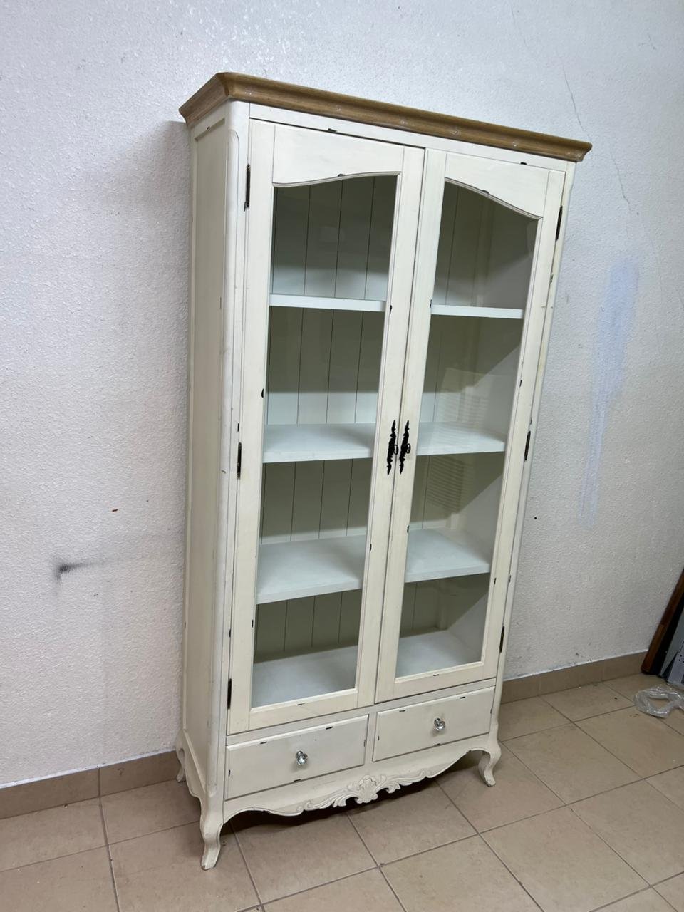 An antique-style display cabinet (vitrine) with two glass doors and an ivory frame with a wooden top.
