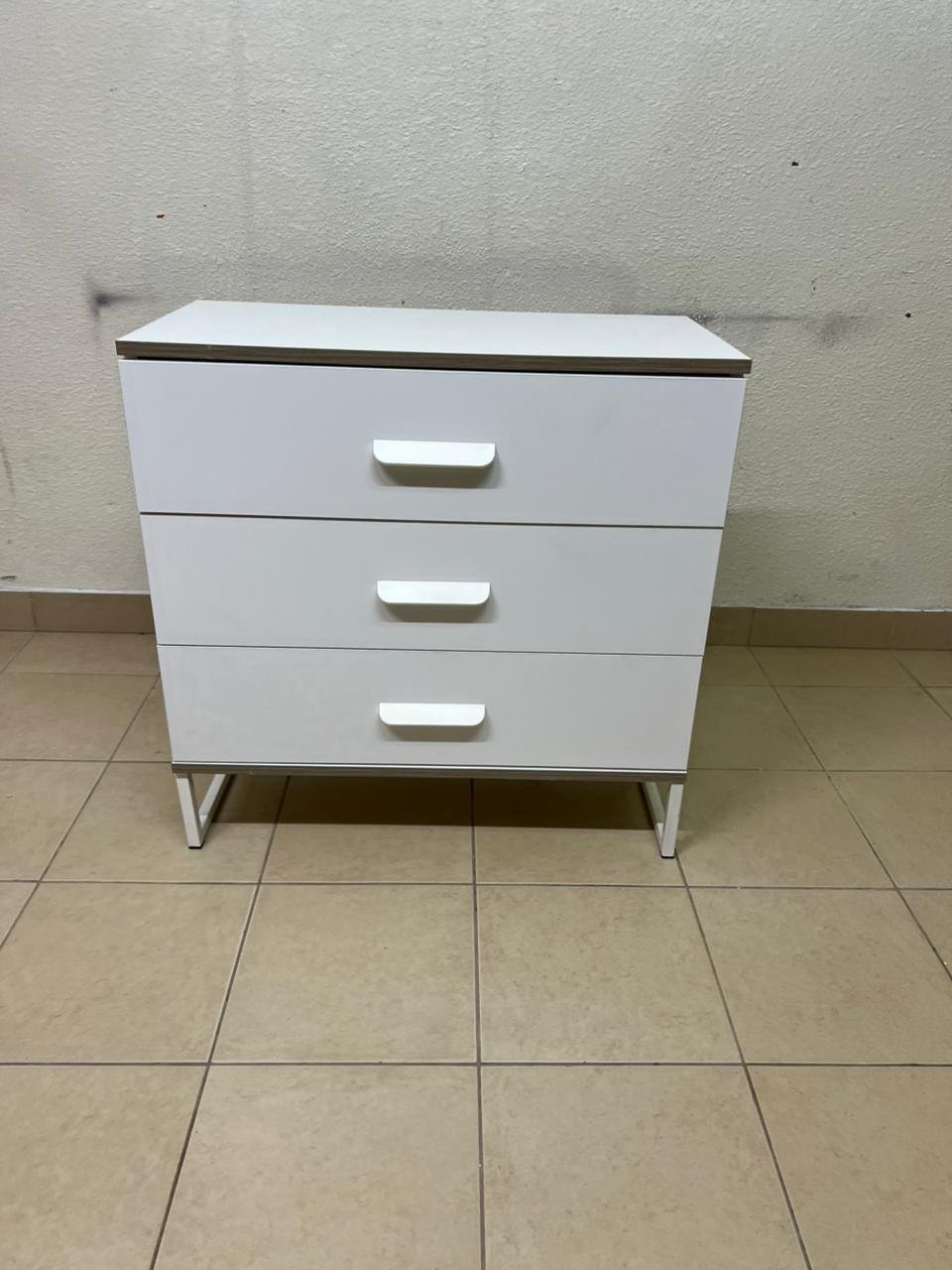 White chest of drawers with three drawers and metal legs with a connected frame.