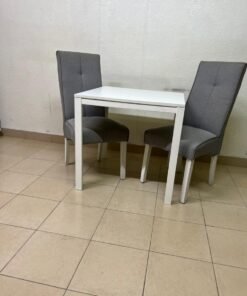 A square white dining table with two chairs