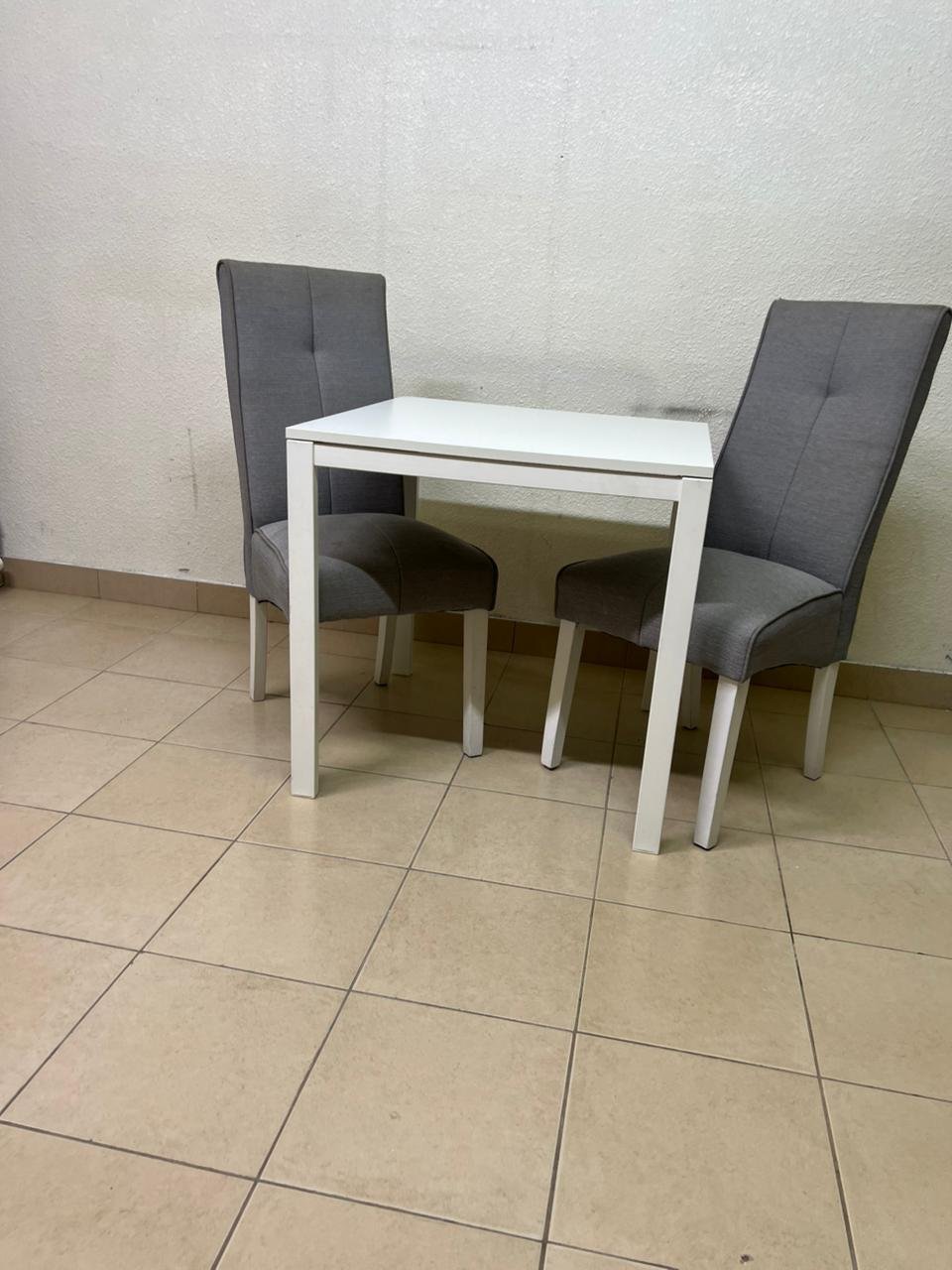 A square white dining table with two chairs
