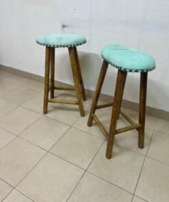 Two wooden bar stools with oval seats upholstered in light turquoise fabric and decorated with nail-like edges.