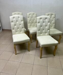 An elegant dining chair upholstered in beige fabric, featuring a high, comfortable back adorned with tufted buttons and delicate metal stud details.