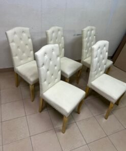 An elegant dining chair upholstered in beige fabric, featuring a high, comfortable back adorned with tufted buttons and delicate metal stud details. - Image 4