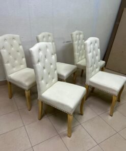 An elegant dining chair upholstered in beige fabric, featuring a high, comfortable back adorned with tufted buttons and delicate metal stud details. - Image 6