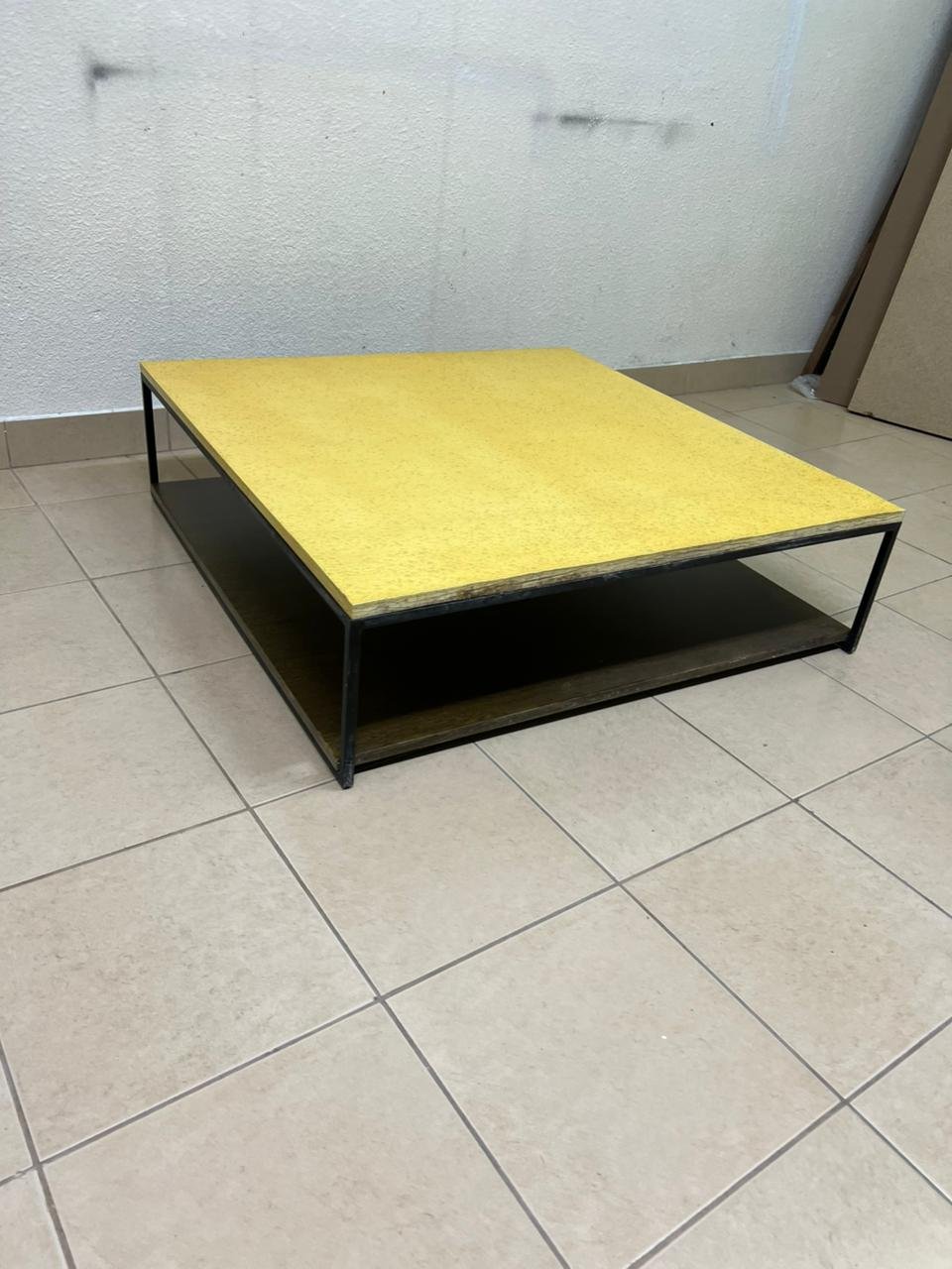This is a square coffee table with an industrial design, featuring a black metal frame, a black pull-out drawer or lower shelf, and a light yellow wooden top. - Image 9