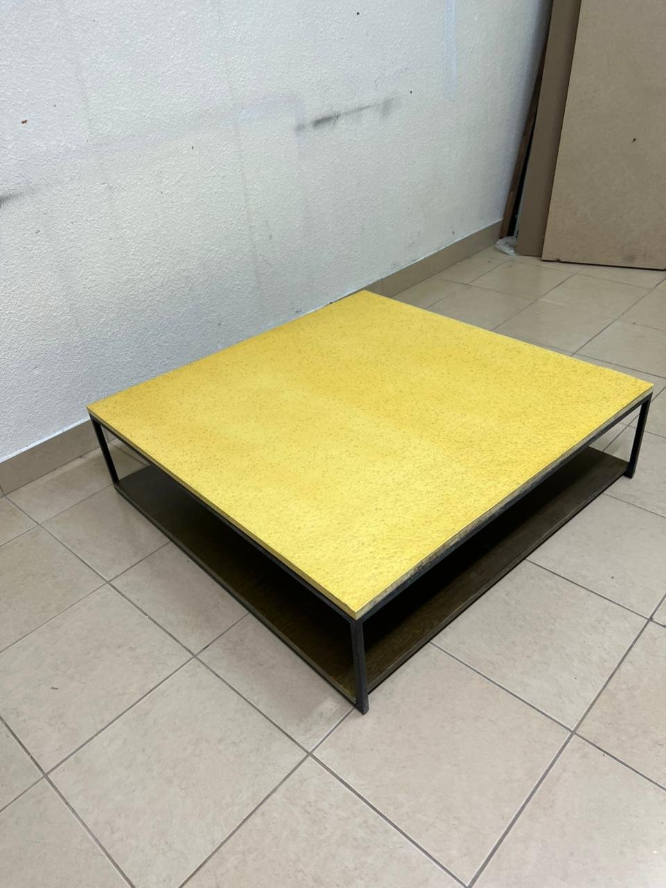 This is a square coffee table with an industrial design, featuring a black metal frame, a black pull-out drawer or lower shelf, and a light yellow wooden top. - Image 3
