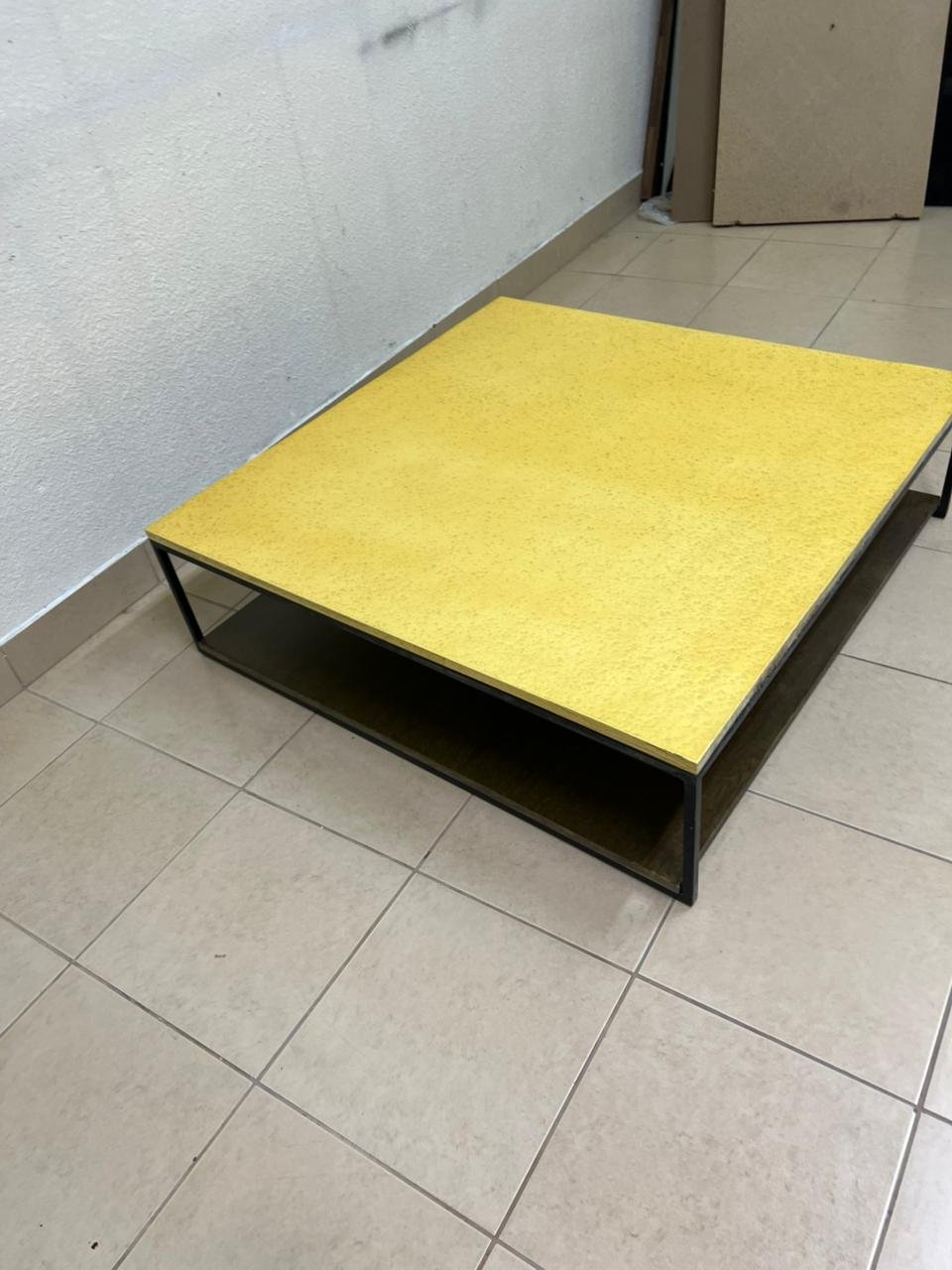 This is a square coffee table with an industrial design, featuring a black metal frame, a black pull-out drawer or lower shelf, and a light yellow wooden top. - Image 4