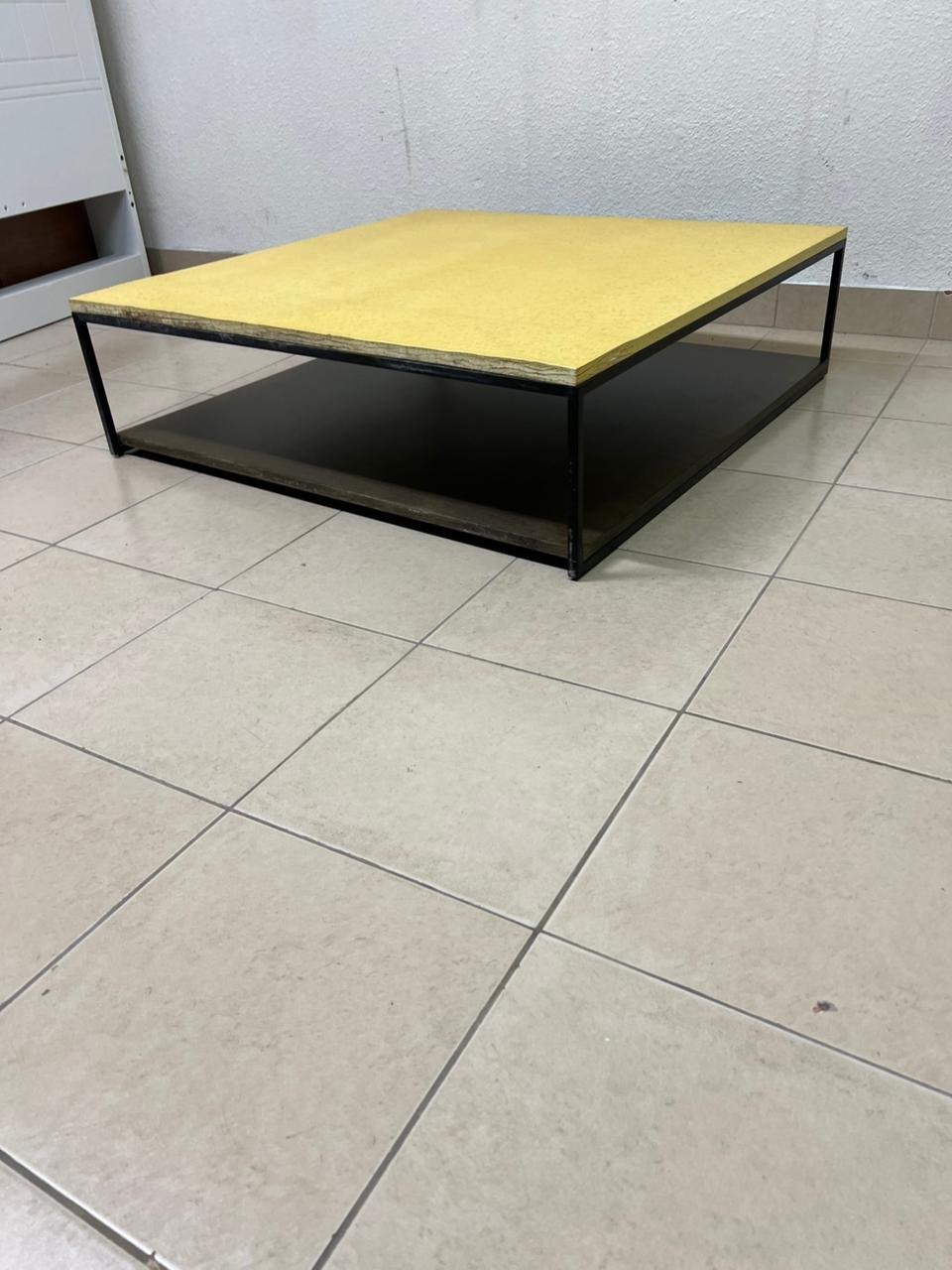 This is a square coffee table with an industrial design, featuring a black metal frame, a black pull-out drawer or lower shelf, and a light yellow wooden top. - Image 5