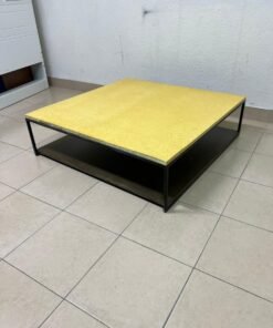 This is a square coffee table with an industrial design, featuring a black metal frame, a black pull-out drawer or lower shelf, and a light yellow wooden top.