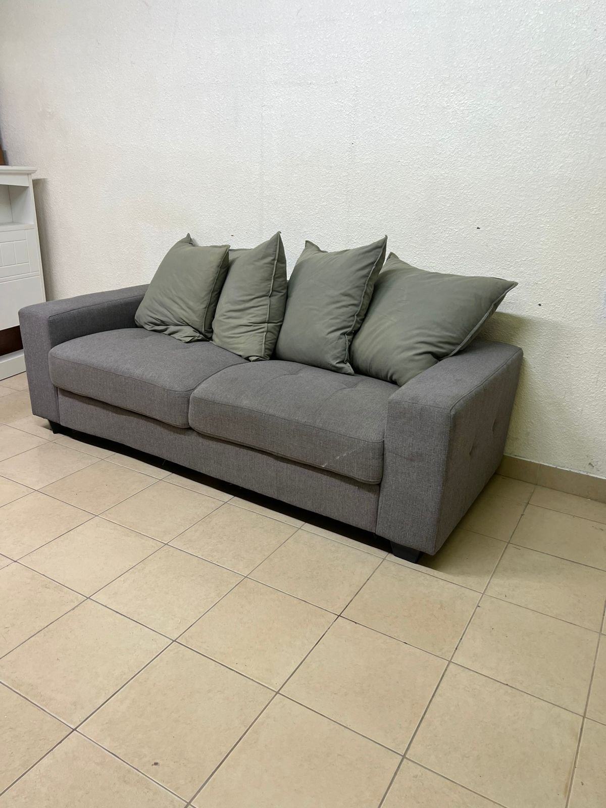 A gray fabric sofa with three seats and a rectangular design, equipped with four olive green back cushions.