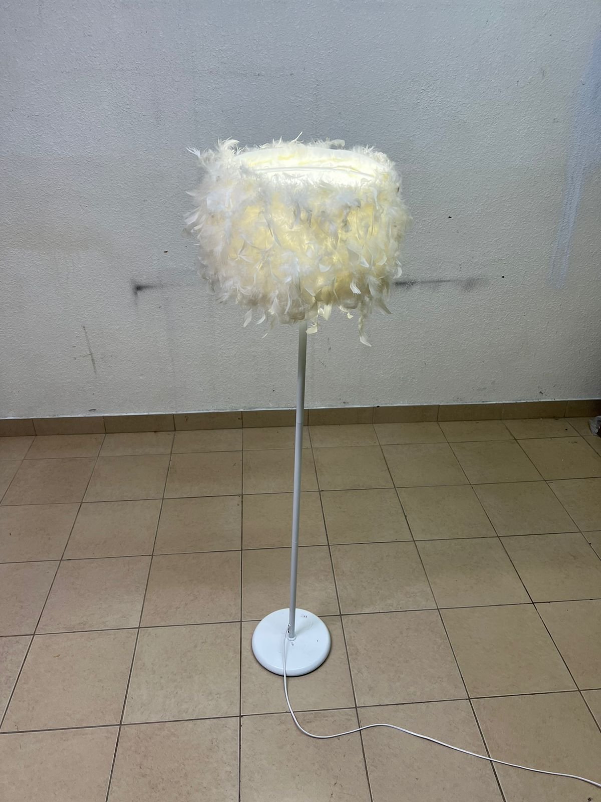 A modern floor lamp featuring a stylish cylindrical shade made of soft white feathers with a white metal base and pole.
