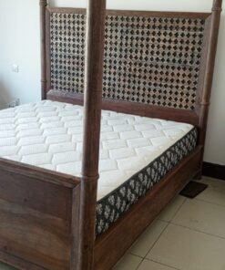 A bed, a piece of wooden furniture with a four-poster design and a headboard decorated with raised geometric patterns, along with a mattress.