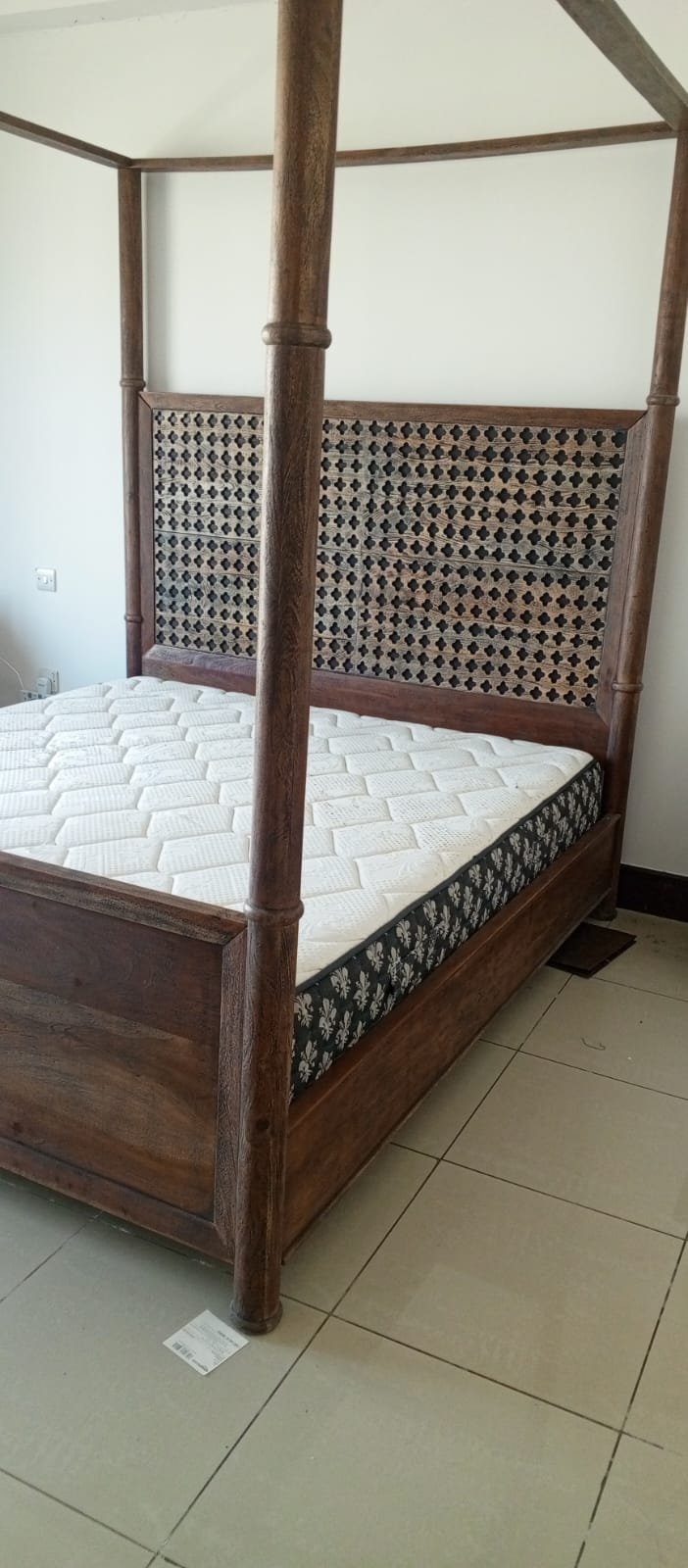 A bed, a piece of wooden furniture with a four-poster design and a headboard decorated with raised geometric patterns, along with a mattress.