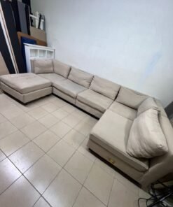 A spacious, modern, U-shaped sectional sofa in a calm beige color with a footrest.