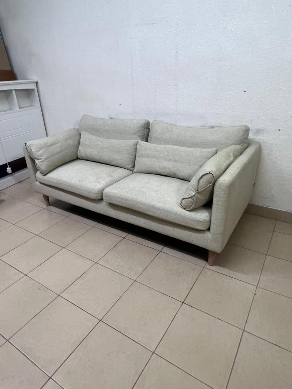 A spacious light beige fabric sofa with back cushions and additional long, square cushions.