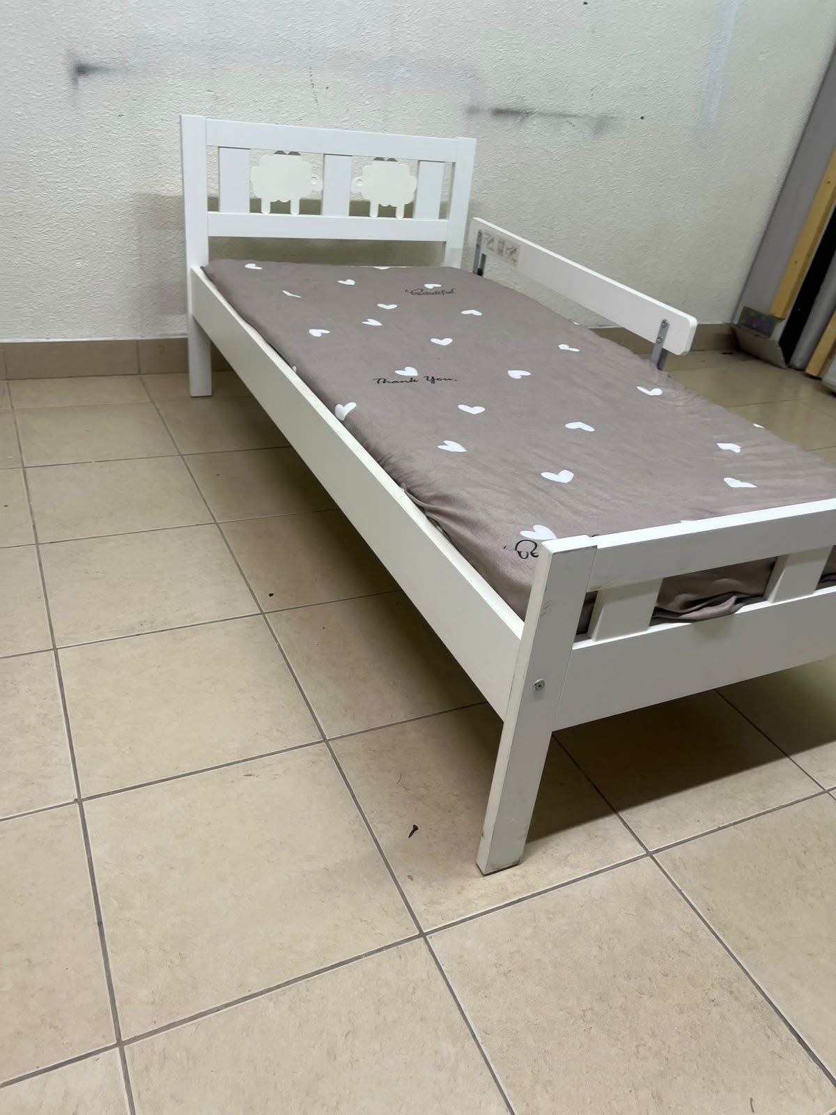 A white wooden cot, believed to be the KRITTER model from IKEA UAE, measuring approximately 70 x 160 cm, and comes with a side guard rail