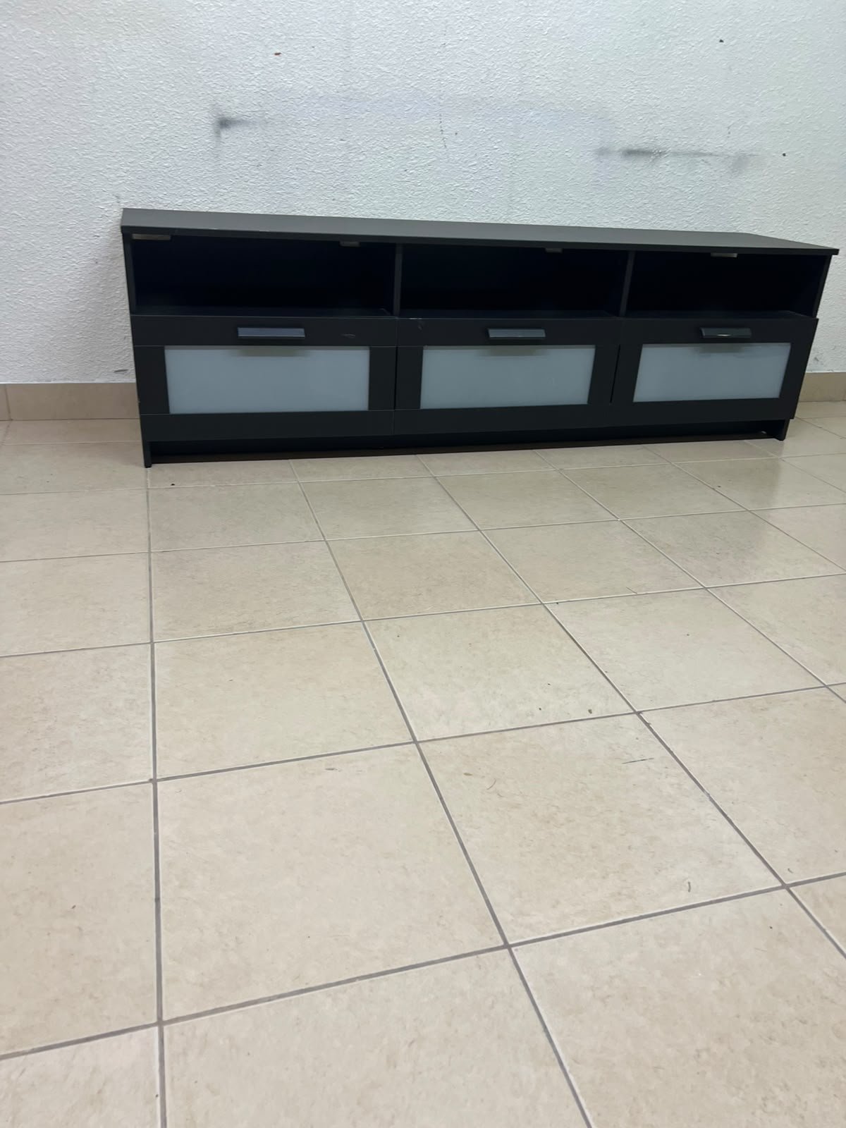 The television unit shown in the picture is a modern black TV stand with three drawers featuring opaque glass fronts and open shelves for appliances. - Image 2