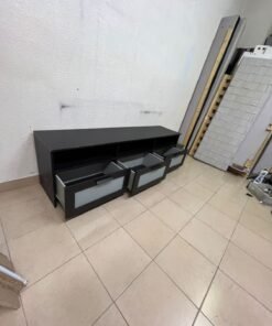 The television unit shown in the picture is a modern black TV stand with three drawers featuring opaque glass fronts and open shelves for appliances. - Image 3