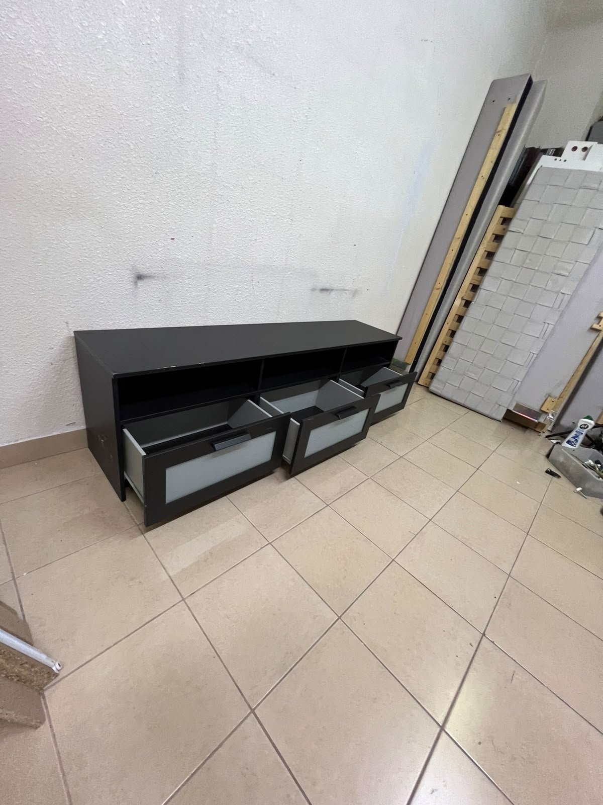 The television unit shown in the picture is a modern black TV stand with three drawers featuring opaque glass fronts and open shelves for appliances. - Image 3
