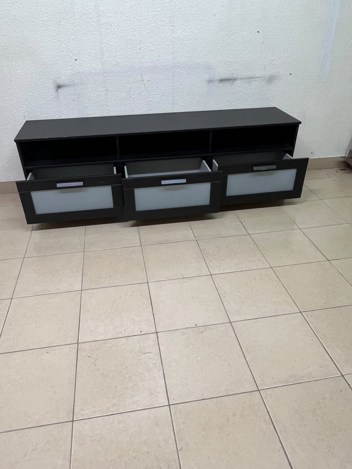 The television unit shown in the picture is a modern black TV stand with three drawers featuring opaque glass fronts and open shelves for appliances. - Image 5