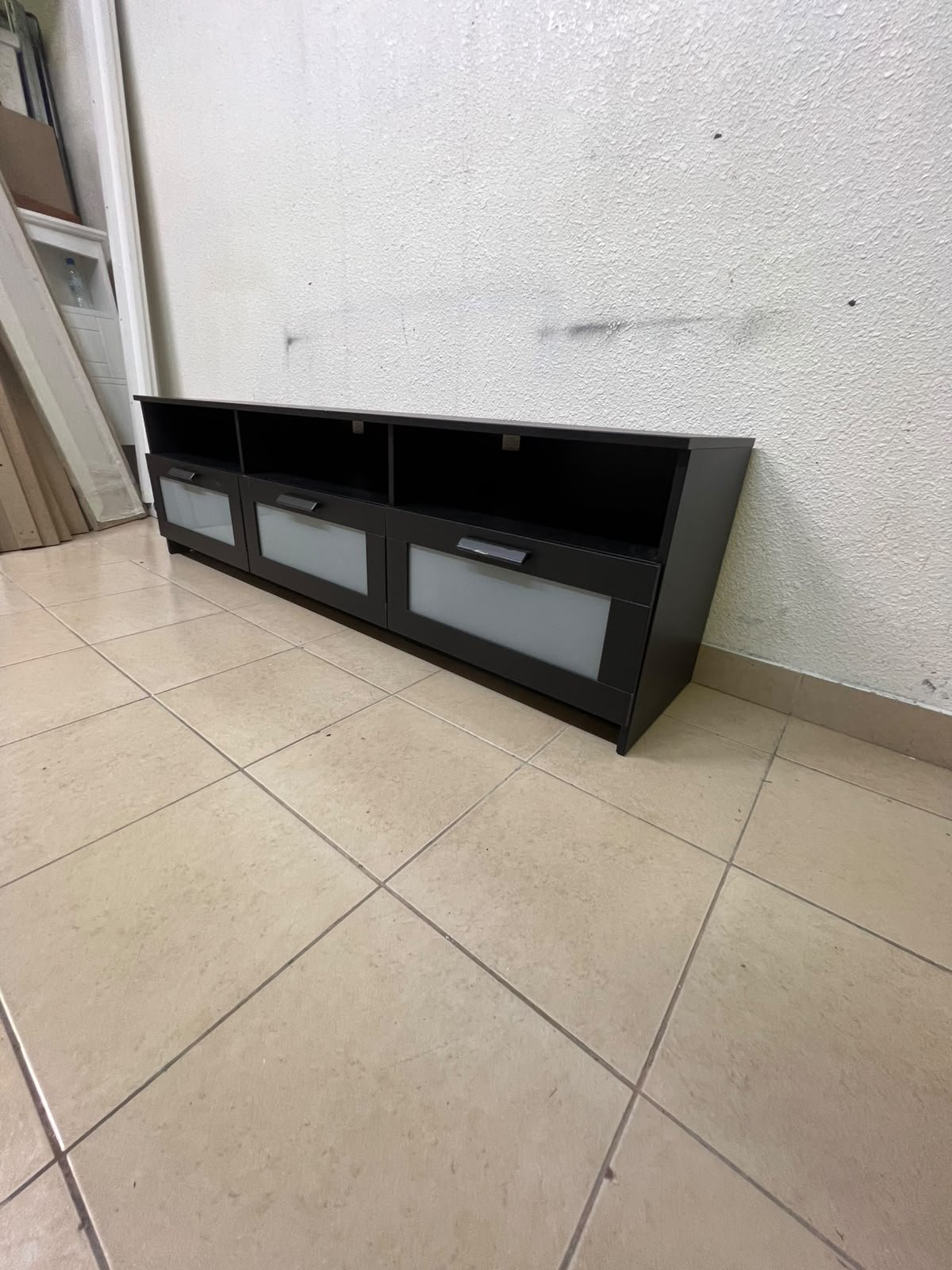 The television unit shown in the picture is a modern black TV stand with three drawers featuring opaque glass fronts and open shelves for appliances. - Image 9