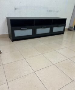 The television unit shown in the picture is a modern black TV stand with three drawers featuring opaque glass fronts and open shelves for appliances.