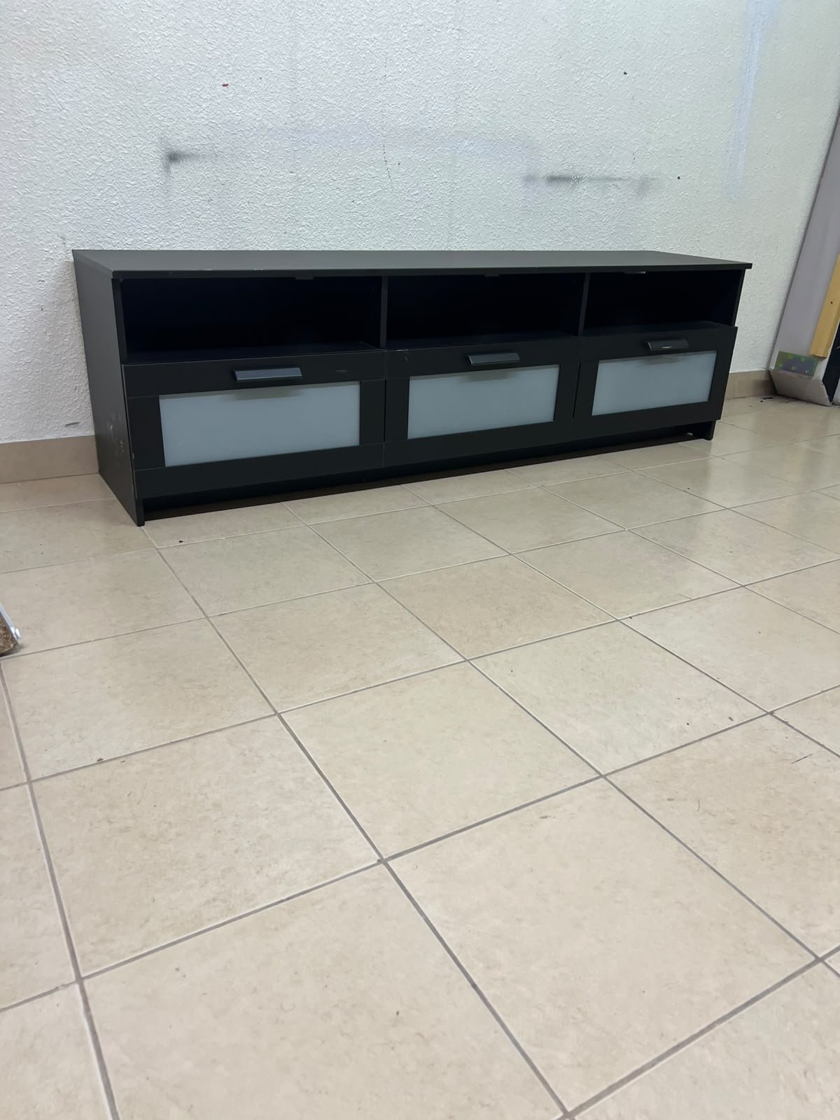 The television unit shown in the picture is a modern black TV stand with three drawers featuring opaque glass fronts and open shelves for appliances.