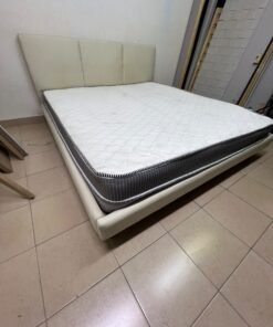 Double bed with a light beige upholstered design, featuring a split headboard and a white mattress with gray and black edges.