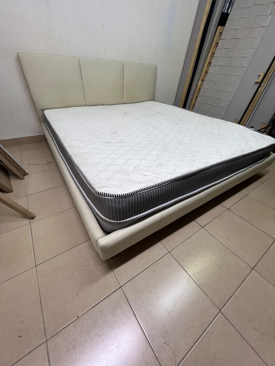 Double bed with a light beige upholstered design, featuring a split headboard and a white mattress with gray and black edges.